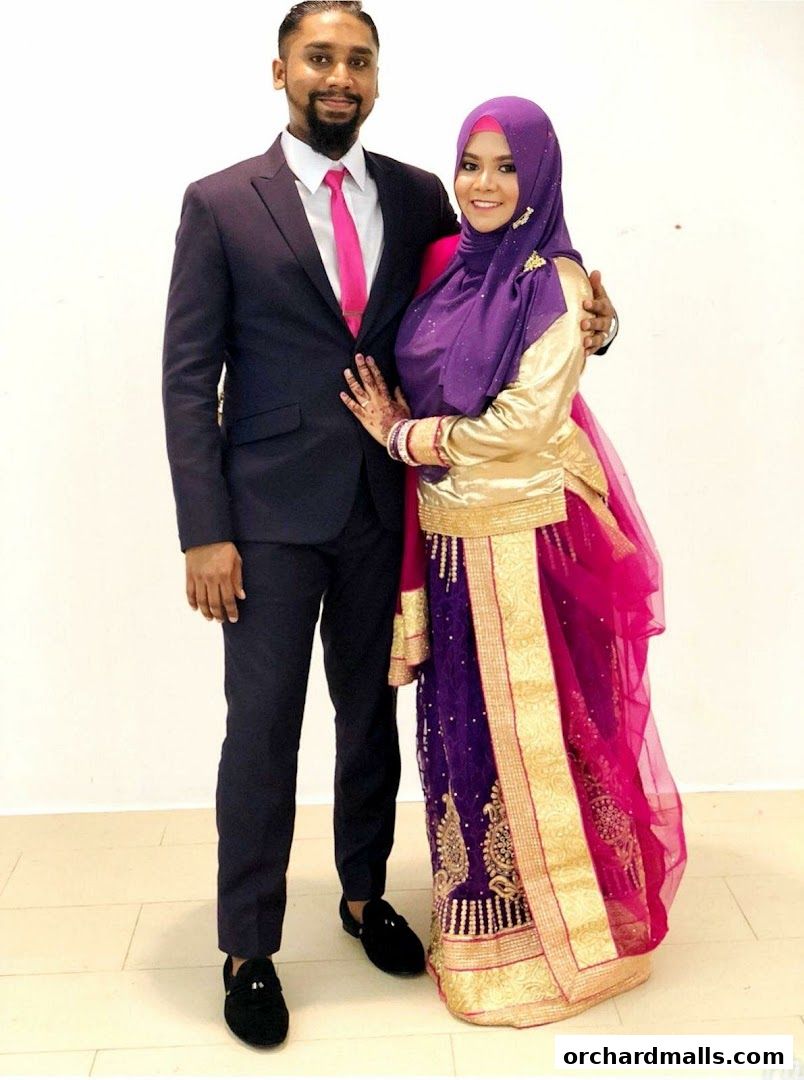 A couple dressed in formal and traditional attire poses for a photo.