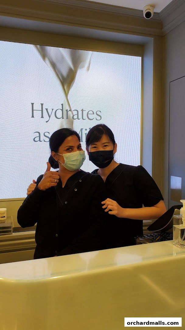 Two smiling staff members in black uniforms and face masks at the Elemis London counter.