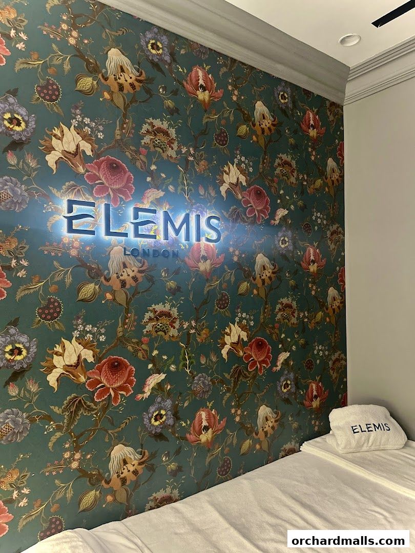 Elemis London logo illuminated on a floral wallpaper with a folded towel.