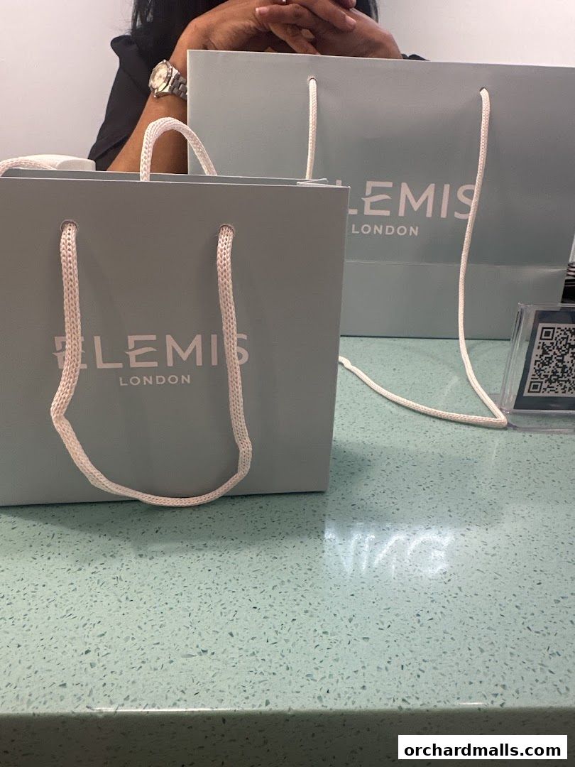 Two light blue shopping bags with the Elemis London logo are on a counter.