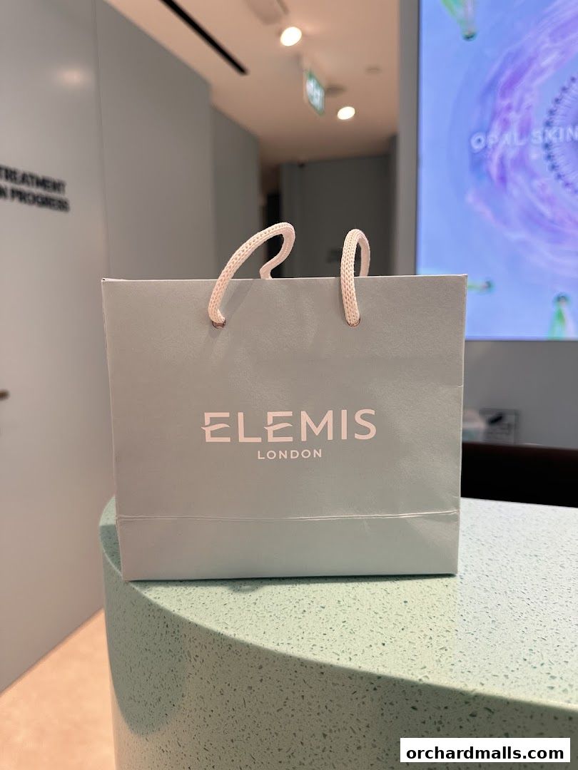 A light blue shopping bag with the Elemis London logo sits on a counter.
