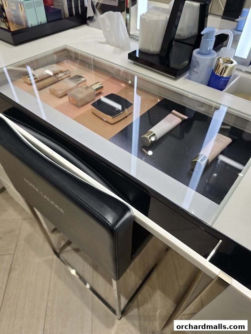 Estée Lauder counter displaying foundations, primers, and skincare products with a branded chair.