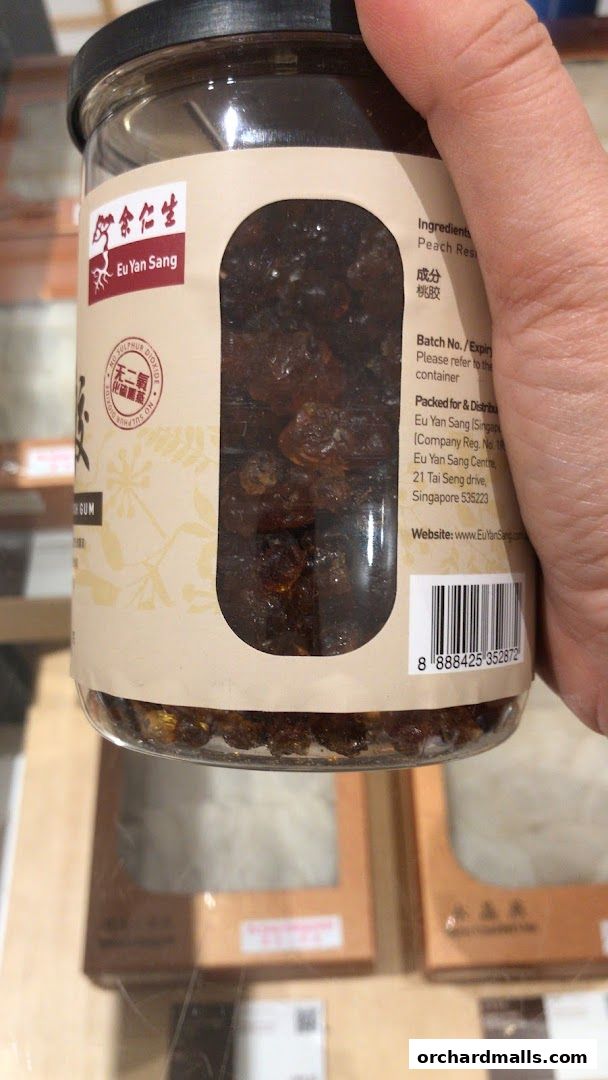 A hand holds a jar of Eu Yan Sang Peach Gum, showing product details and branding.