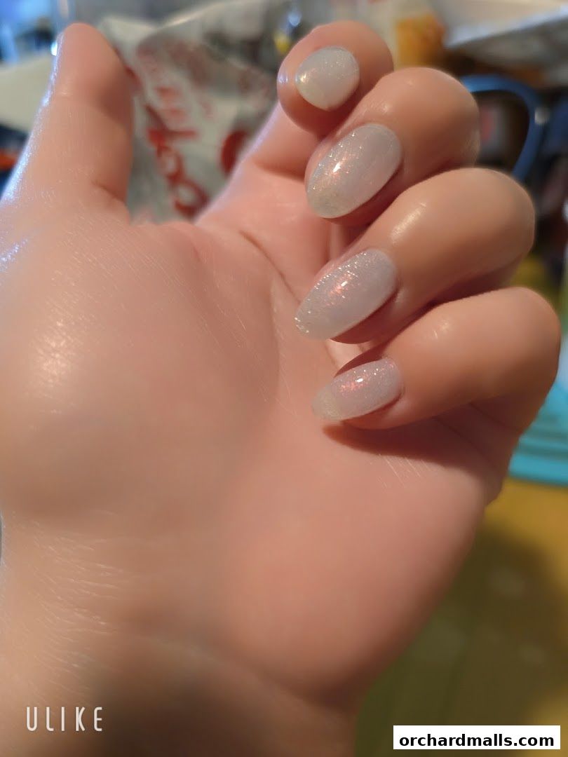 A close-up of a hand with beautifully manicured, shimmering light-colored nails.