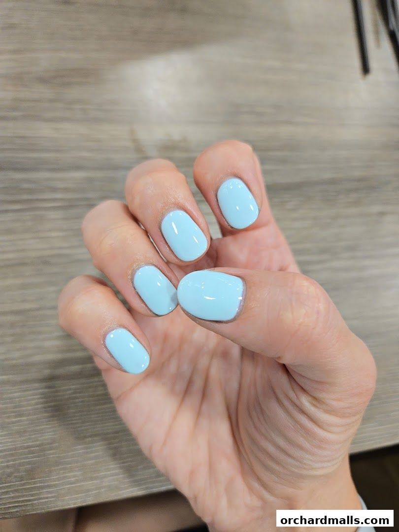 A hand with perfectly manicured light blue nails rests on a wooden surface.