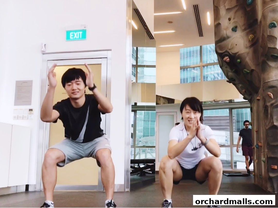 Two people doing squats in a gym with a climbing wall.
