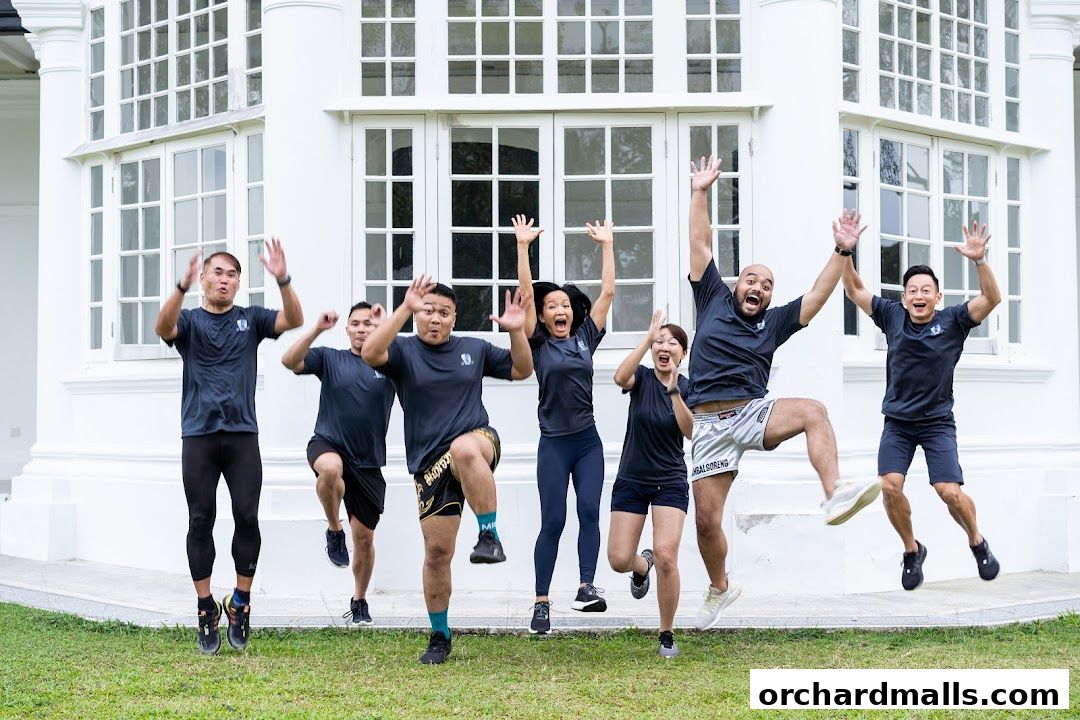A group of people in athletic wear jumping joyfully in front of a white building.