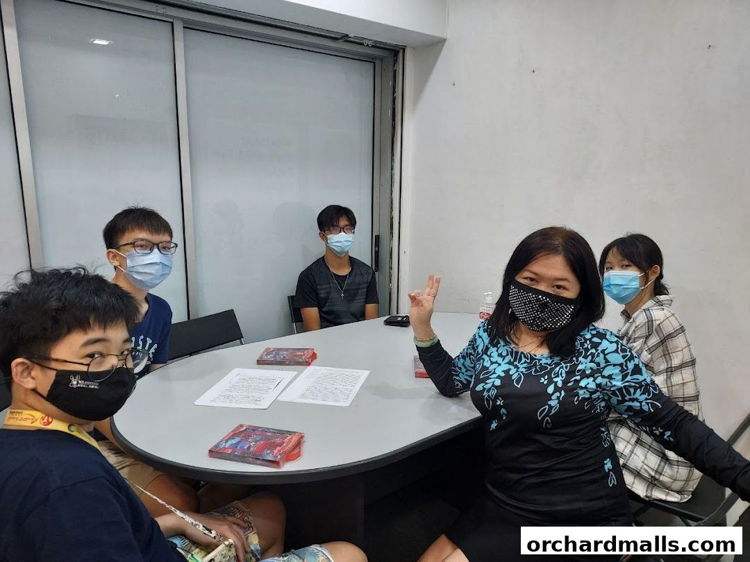 A group of students and a teacher wearing masks sit around a table in a classroom.