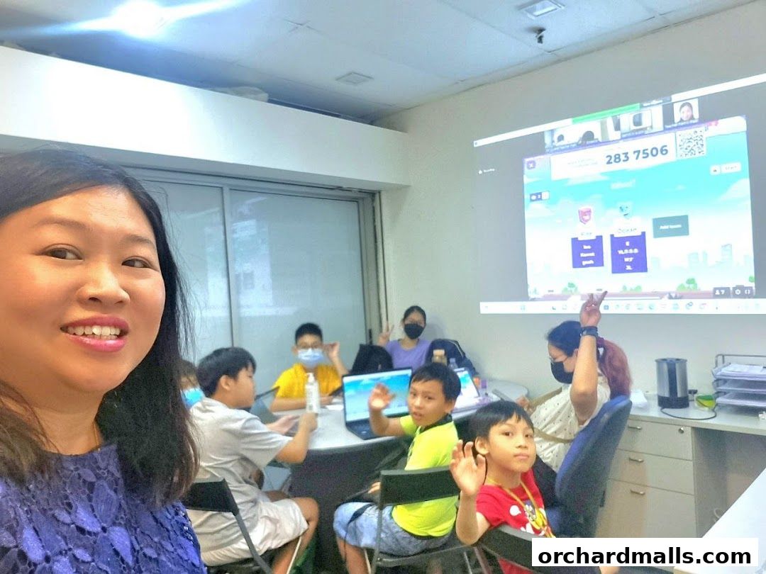 A teacher and students in a classroom setting with a projector screen displaying educational content.
