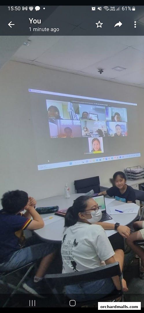 Students participate in an online class projected on a screen in a classroom.