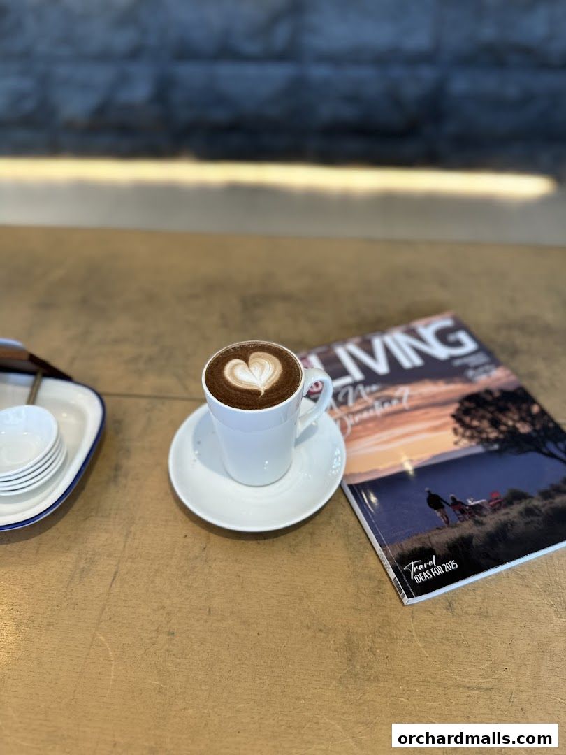 A cup of coffee with latte art sits next to a magazine on a wooden table.