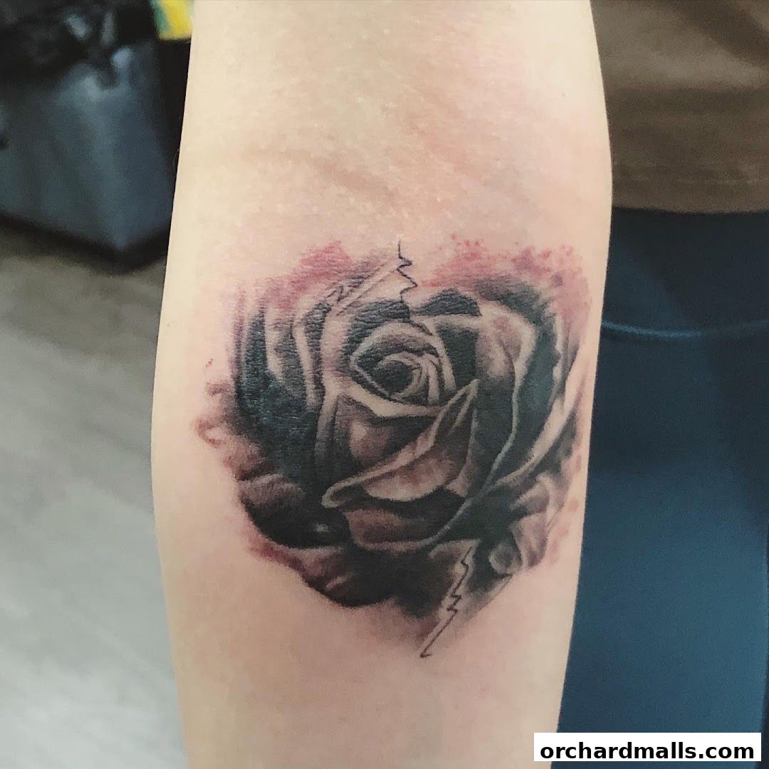 A realistic black and grey rose tattoo with watercolor-like shading on a person's arm.