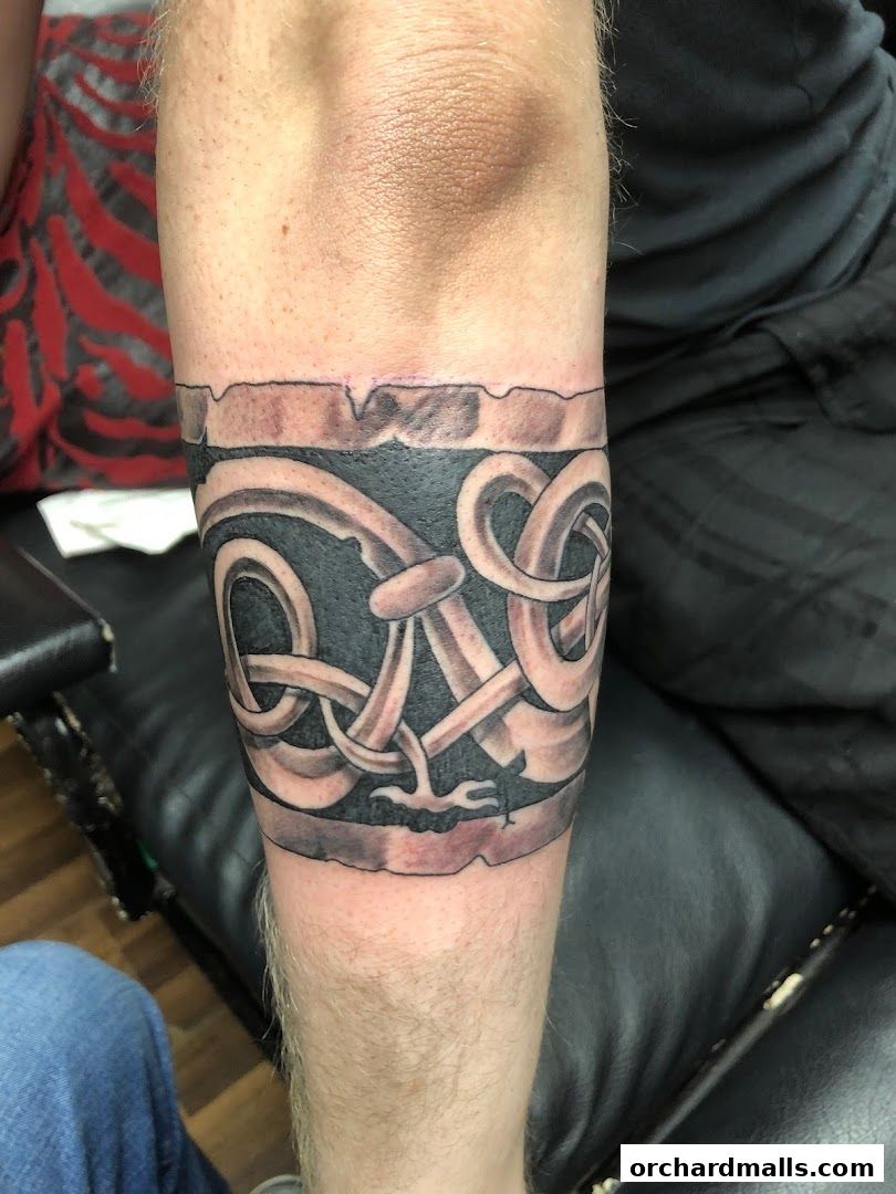 A close-up of a black and grey Celtic knot tattoo on a person's forearm.