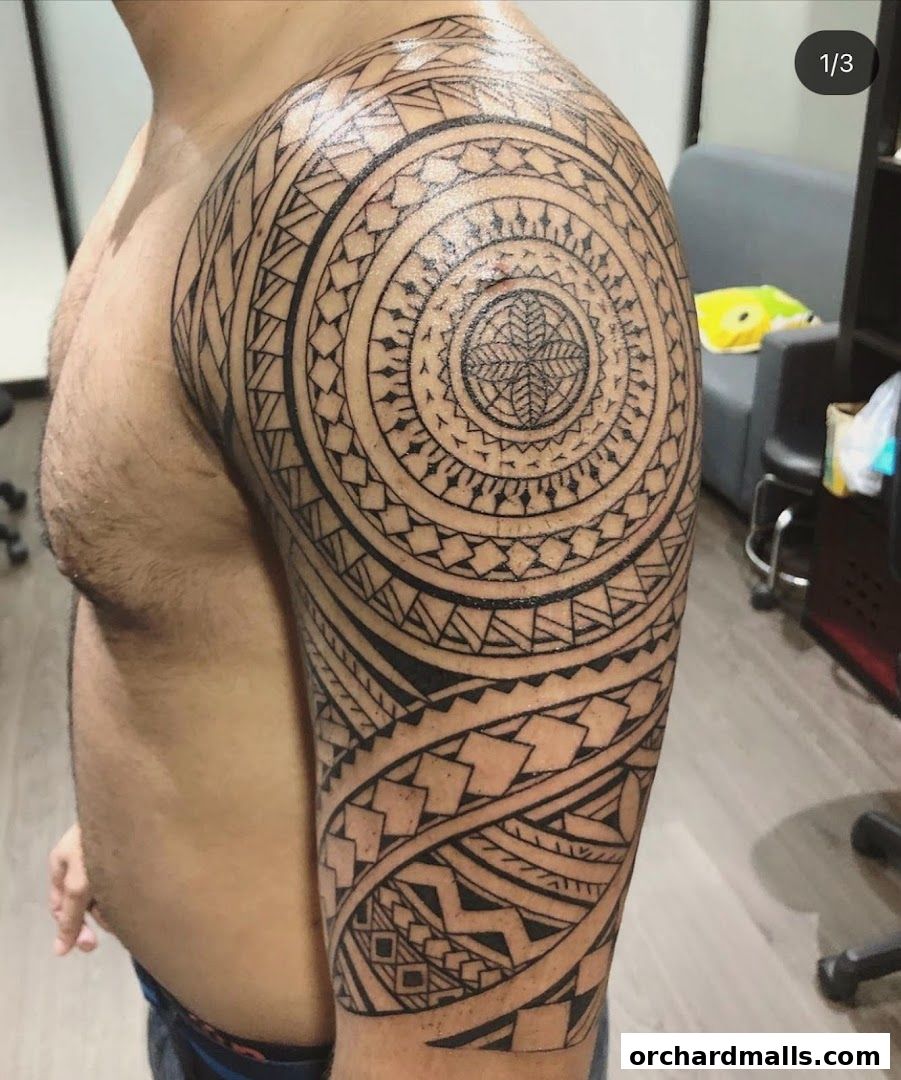 A man's arm displays a detailed black tribal-style tattoo covering the shoulder and upper arm.