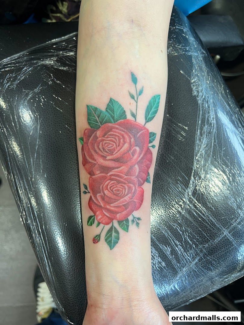 A realistic tattoo of two red roses with green leaves on a person's forearm.
