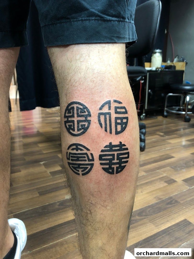 A person's leg displays four intricate black tattoos with traditional Chinese characters.