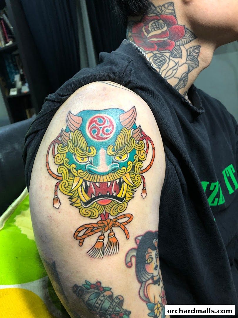 A person displays a colorful, intricate tattoo of a Japanese mask on their arm.