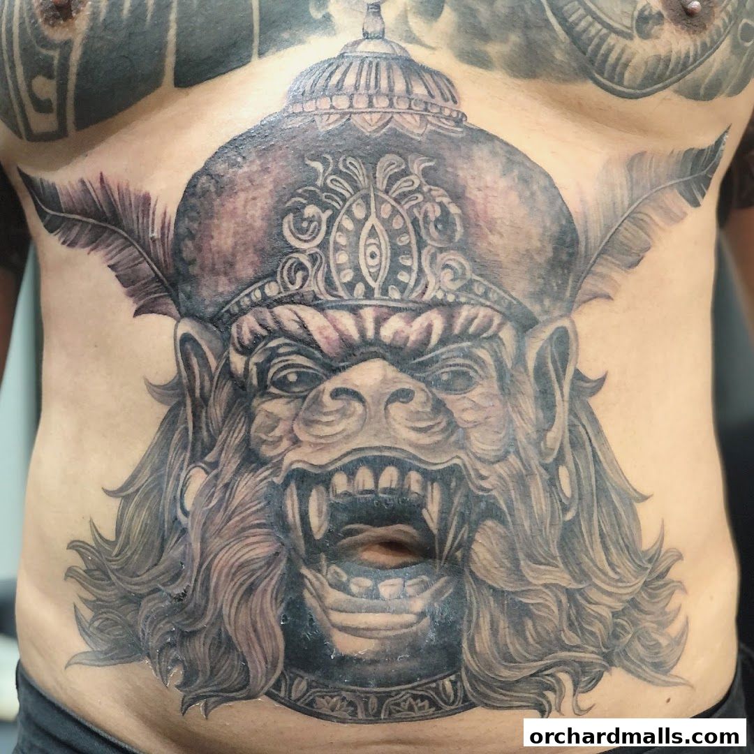 A detailed tattoo of a fierce monkey face wearing a headdress on a person's torso.