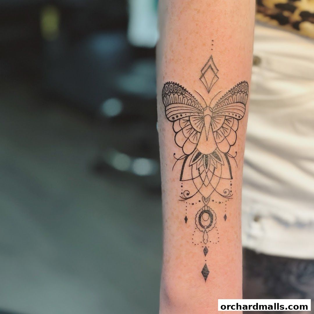 A detailed black ink tattoo of a butterfly with intricate mandala-like patterns on an arm.