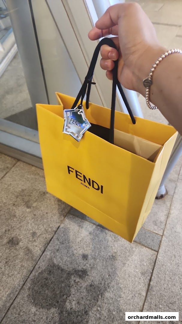 A hand holds a bright yellow Fendi shopping bag with a star-shaped tag.