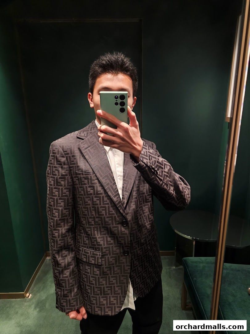 A person in a Fendi branded blazer takes a mirror selfie in a fitting room.