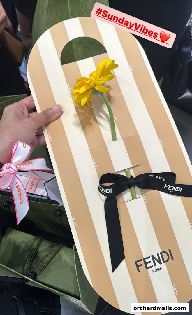 A hand holds a Fendi branded item with a yellow flower and Fendi and Chanel ribbons.