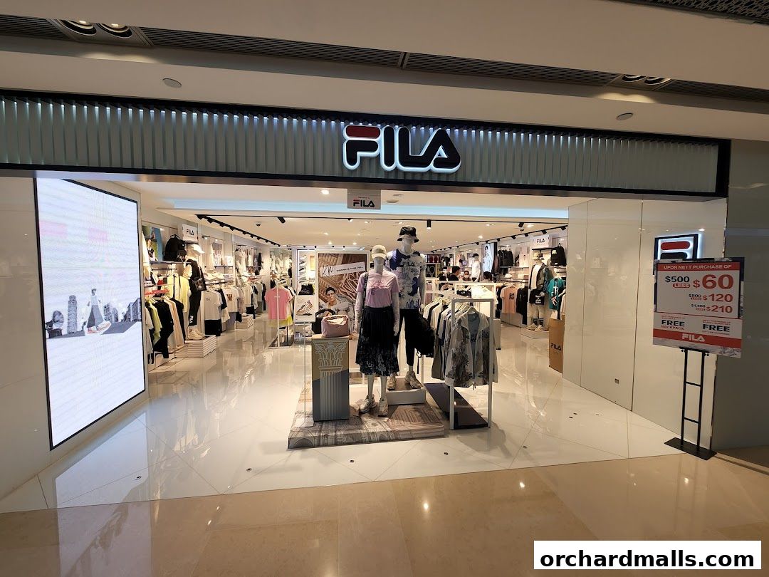 The entrance of a FILA store showcasing apparel on mannequins and racks, with a promotional sign.