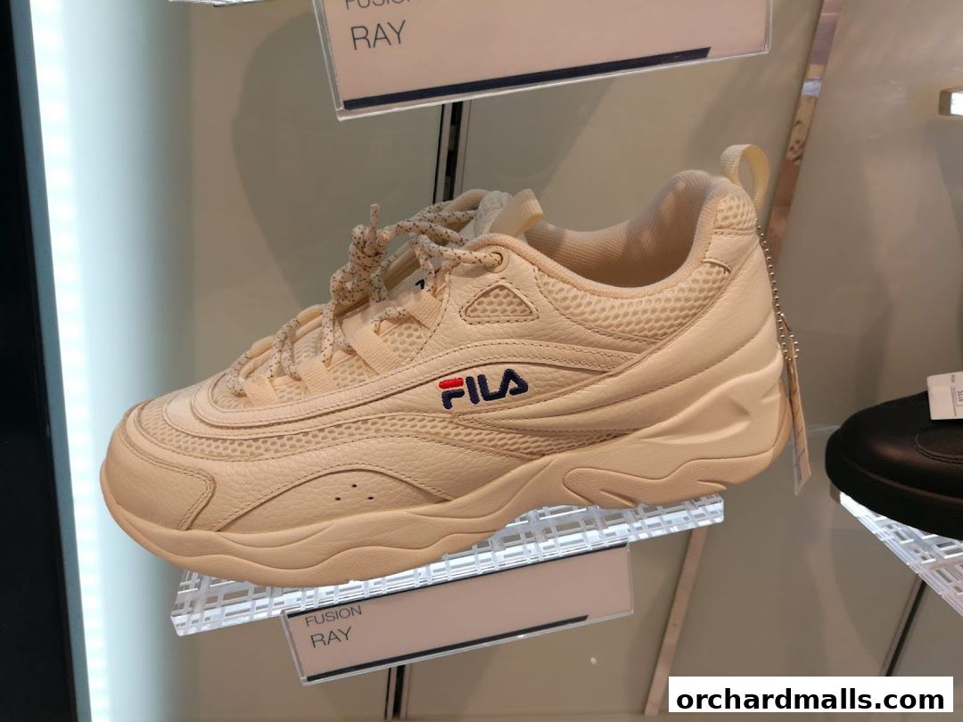 A cream-colored Fila sneaker with a chunky sole is displayed on a shelf.