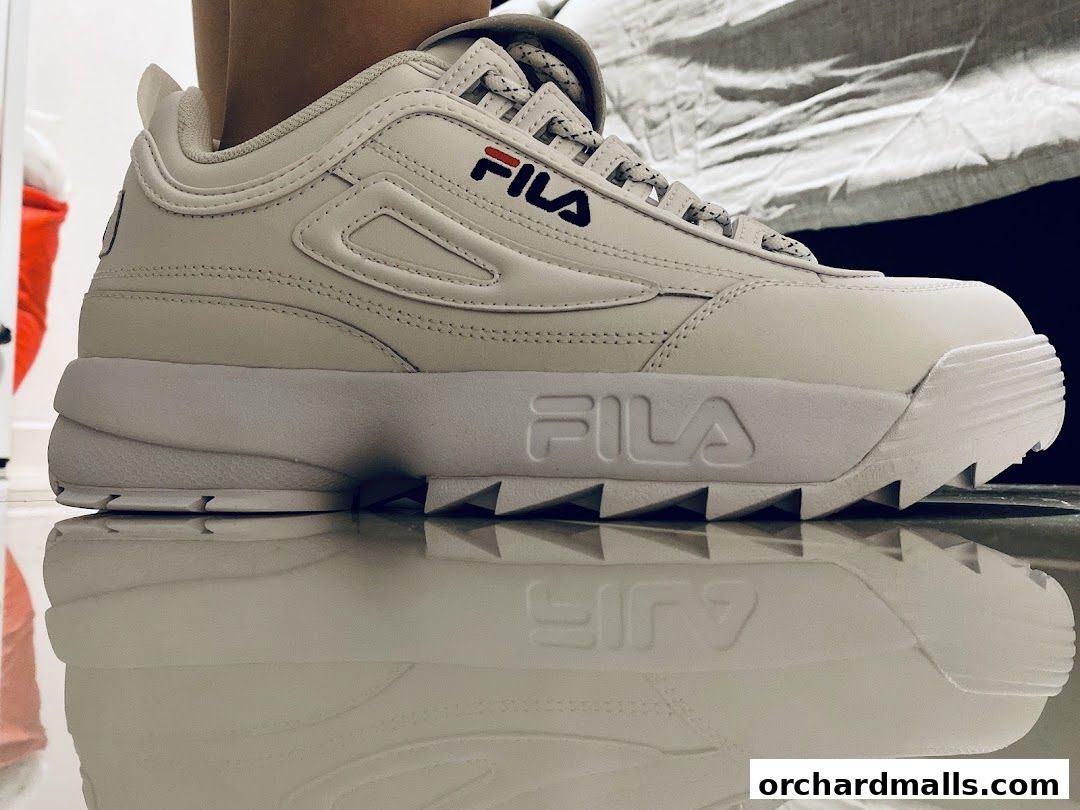 A close-up shot of a white Fila sneaker with its reflection on a shiny surface.