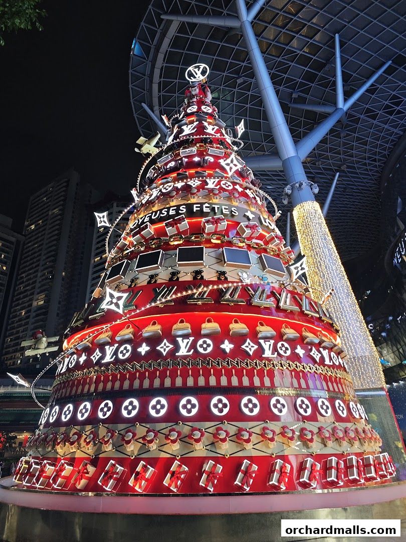 A festive Christmas tree decorated with Louis Vuitton logos and gift boxes at night.