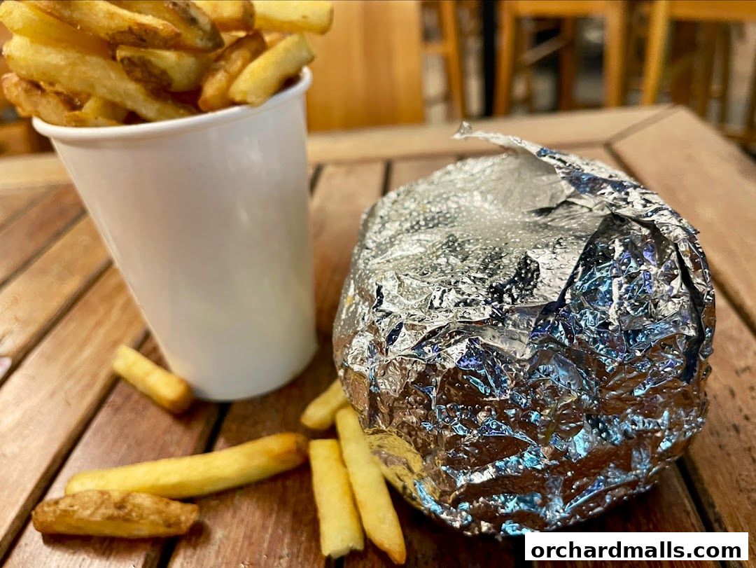 A foil-wrapped burger and a cup of fries sit on a wooden table.