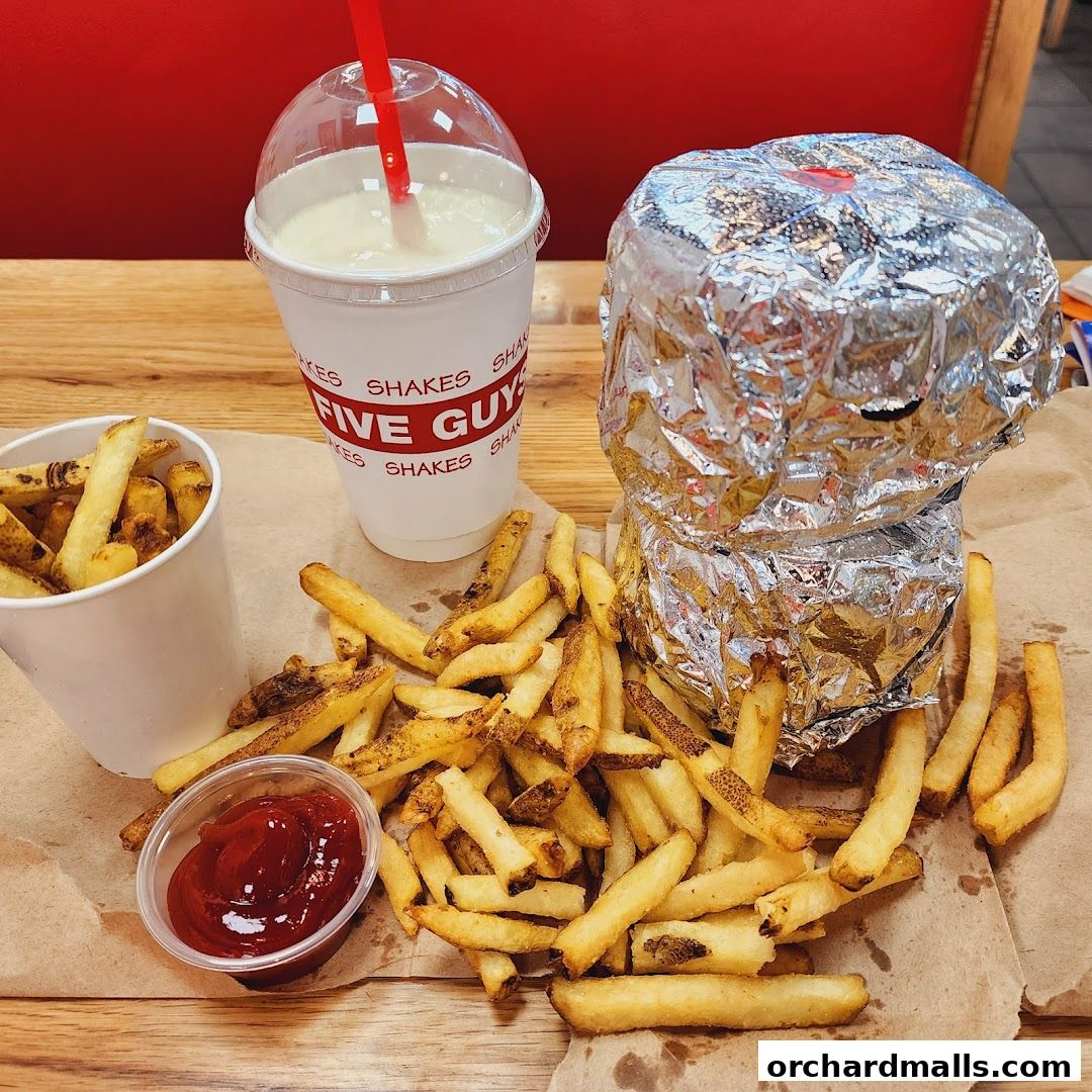 A Five Guys meal featuring a foil-wrapped burger, fries, and a milkshake.