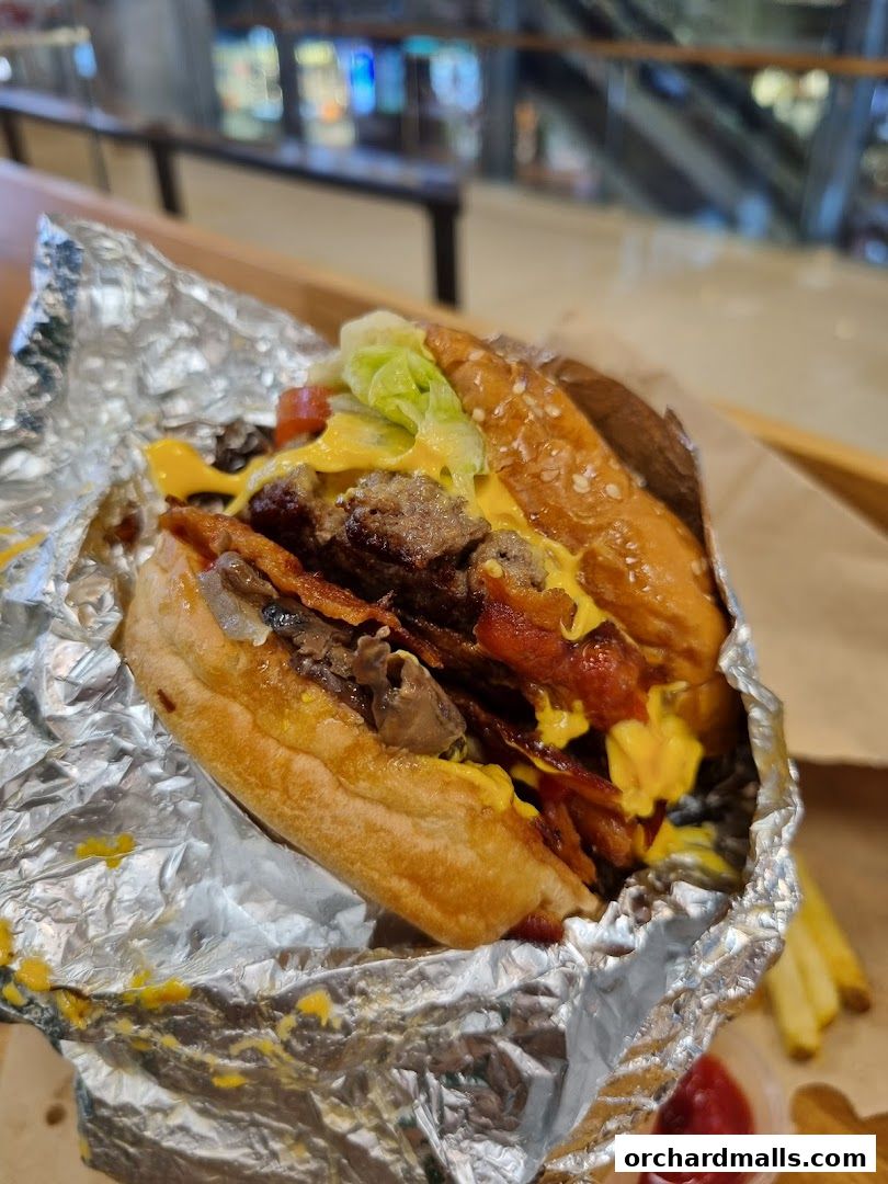 A close-up of a delicious Five Guys burger with bacon, cheese, and lettuce, served in foil.