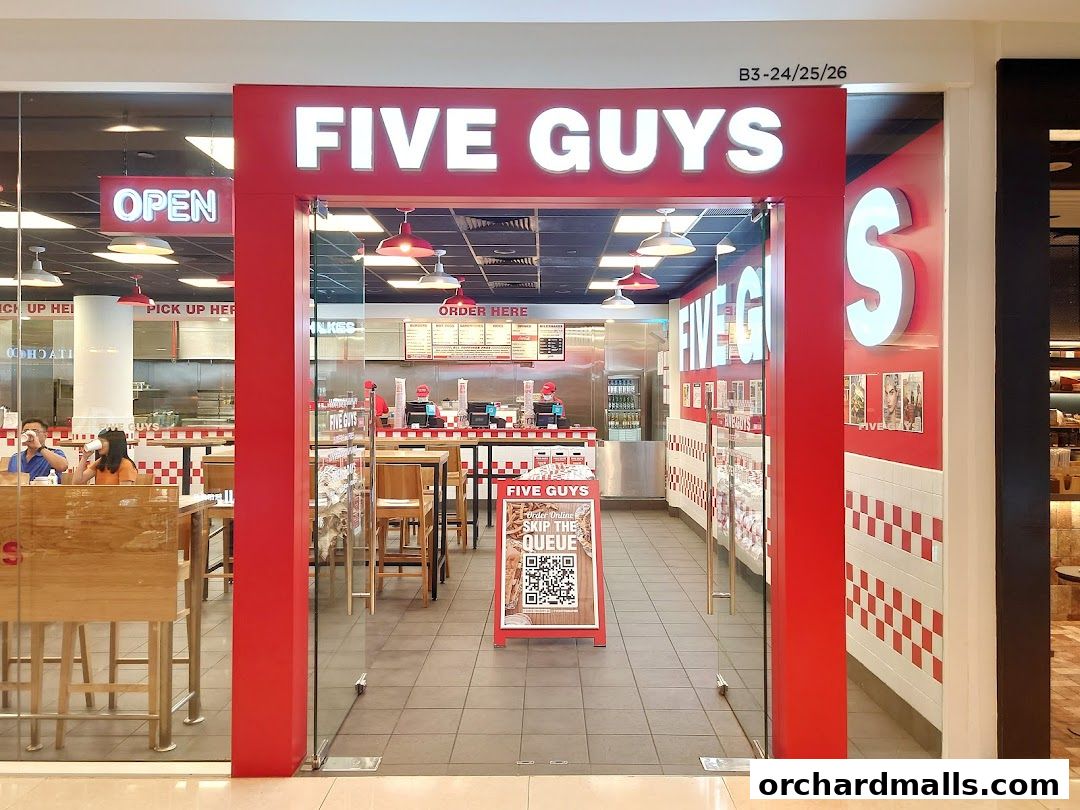 The entrance to a Five Guys restaurant with red and white branding and seating visible inside.