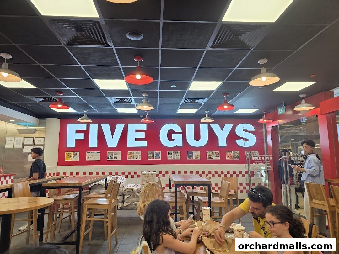 People dining inside a Five Guys restaurant with the brand name prominently displayed.