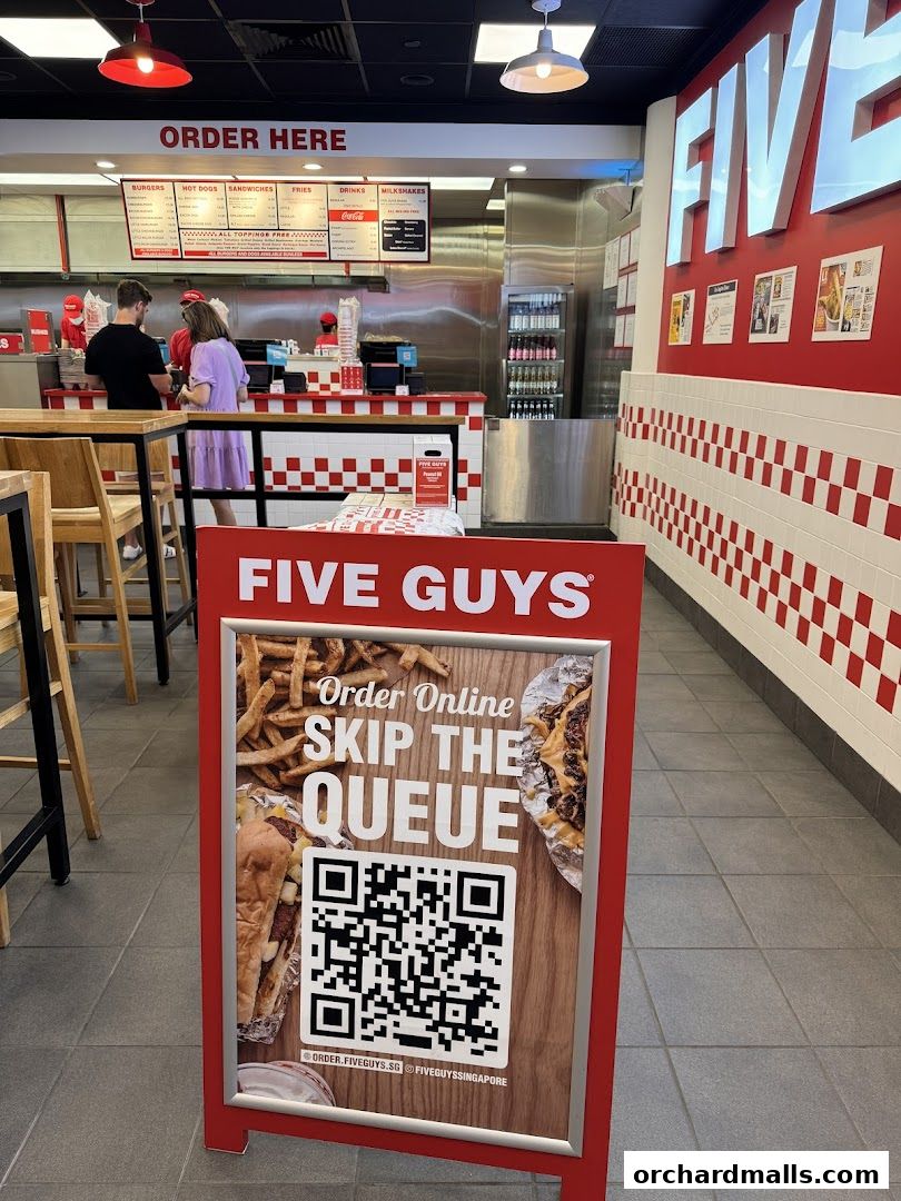 Interior view of a Five Guys restaurant with a prominent 'Order Here' sign and a promotional stand.