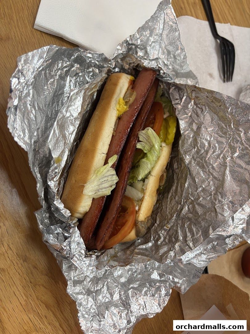 A delicious hot dog with toppings wrapped in foil on a wooden table.