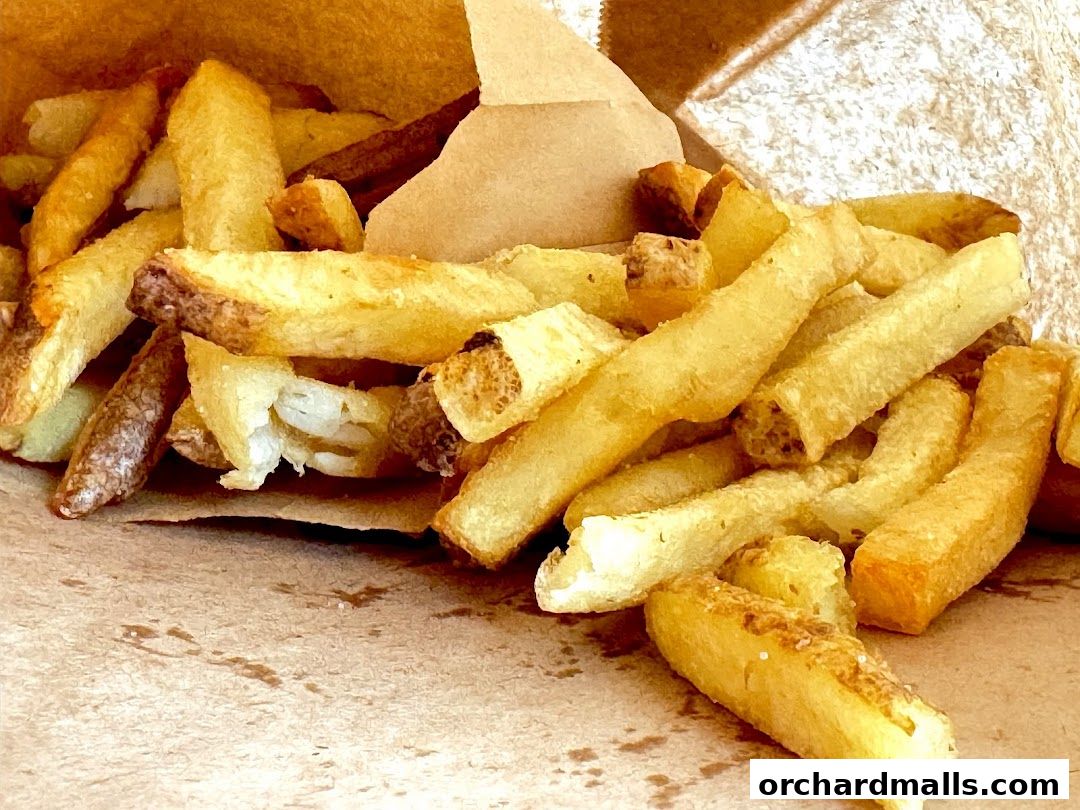 A close-up shot of a generous portion of golden-brown, crispy French fries spilling out of a paper bag.