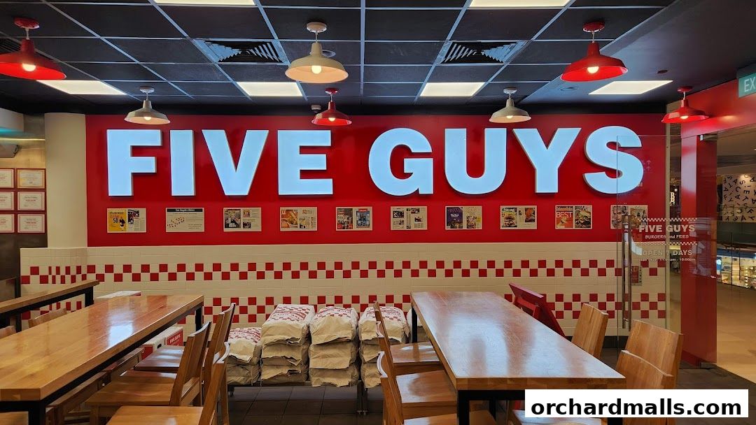 Interior of Five Guys restaurant with large signage, tables, chairs, and bags of fries.