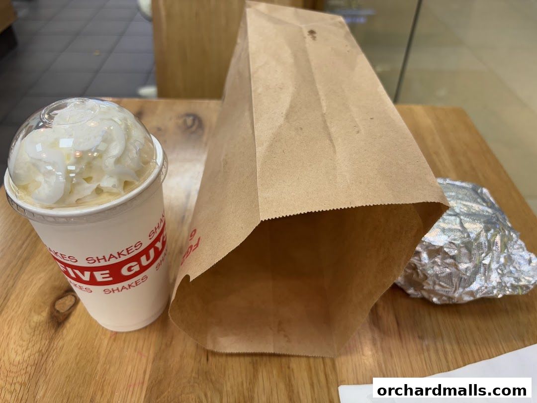 A Five Guys shake, paper bag, and foil-wrapped food on a wooden table.
