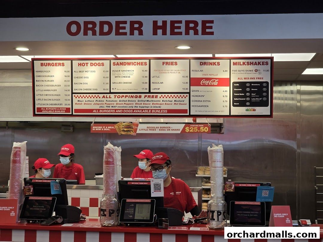 A Five Guys restaurant counter with a menu board displaying burgers, hot dogs, sandwiches, fries, drinks, and milkshakes.