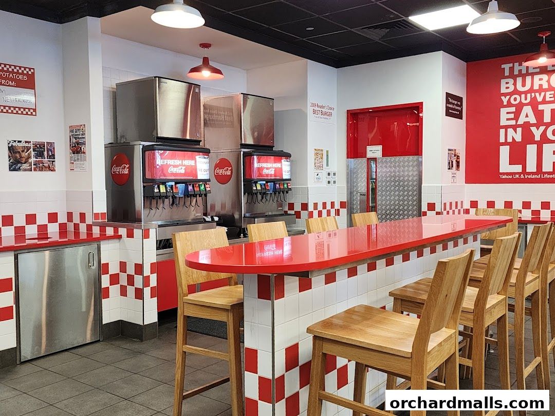 Interior of a Five Guys restaurant with a red counter, bar stools, and soda dispensers.