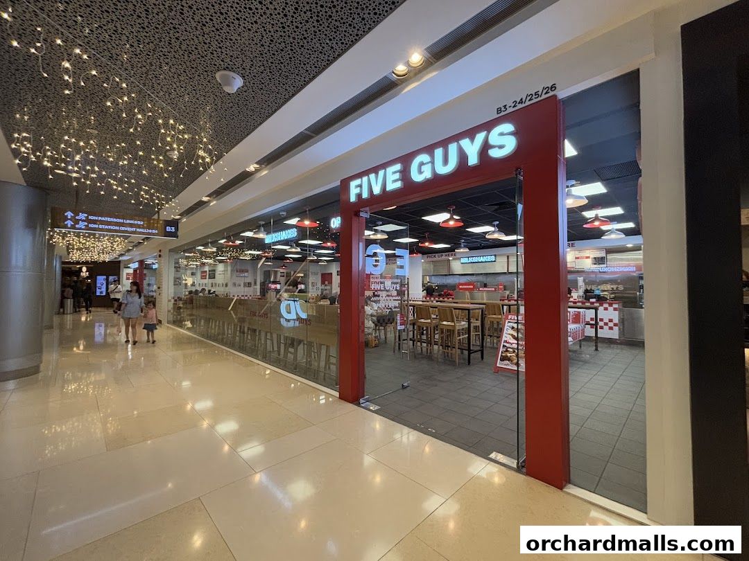 The entrance to a Five Guys restaurant in a shopping mall, with seating visible inside.
