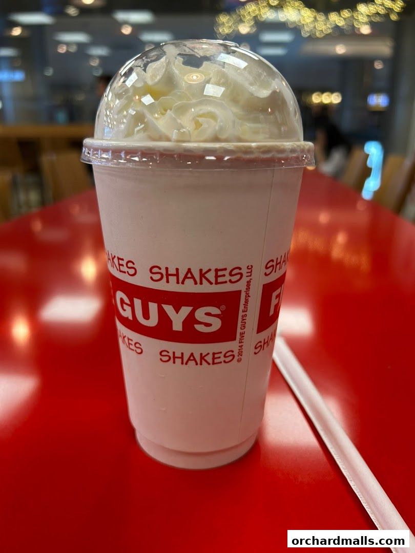 A close-up of a Five Guys shake topped with whipped cream on a red table.