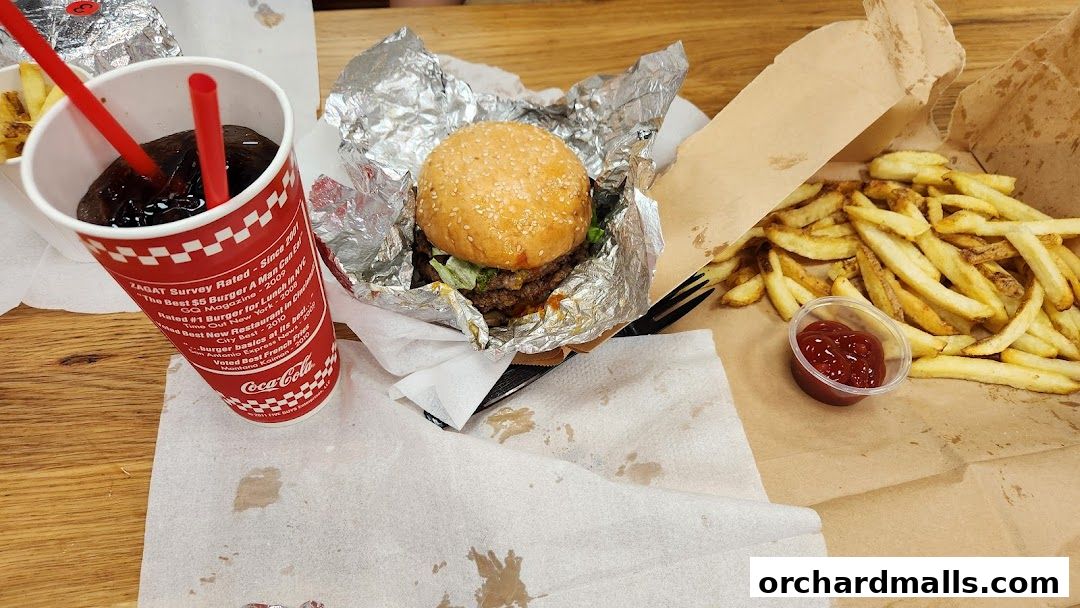 A Five Guys burger, fries, and a soda with two straws on a wooden table.