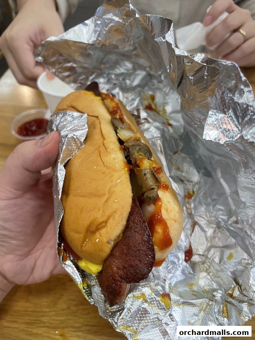 A person holds a foil-wrapped hot dog with toppings and a side of ketchup.