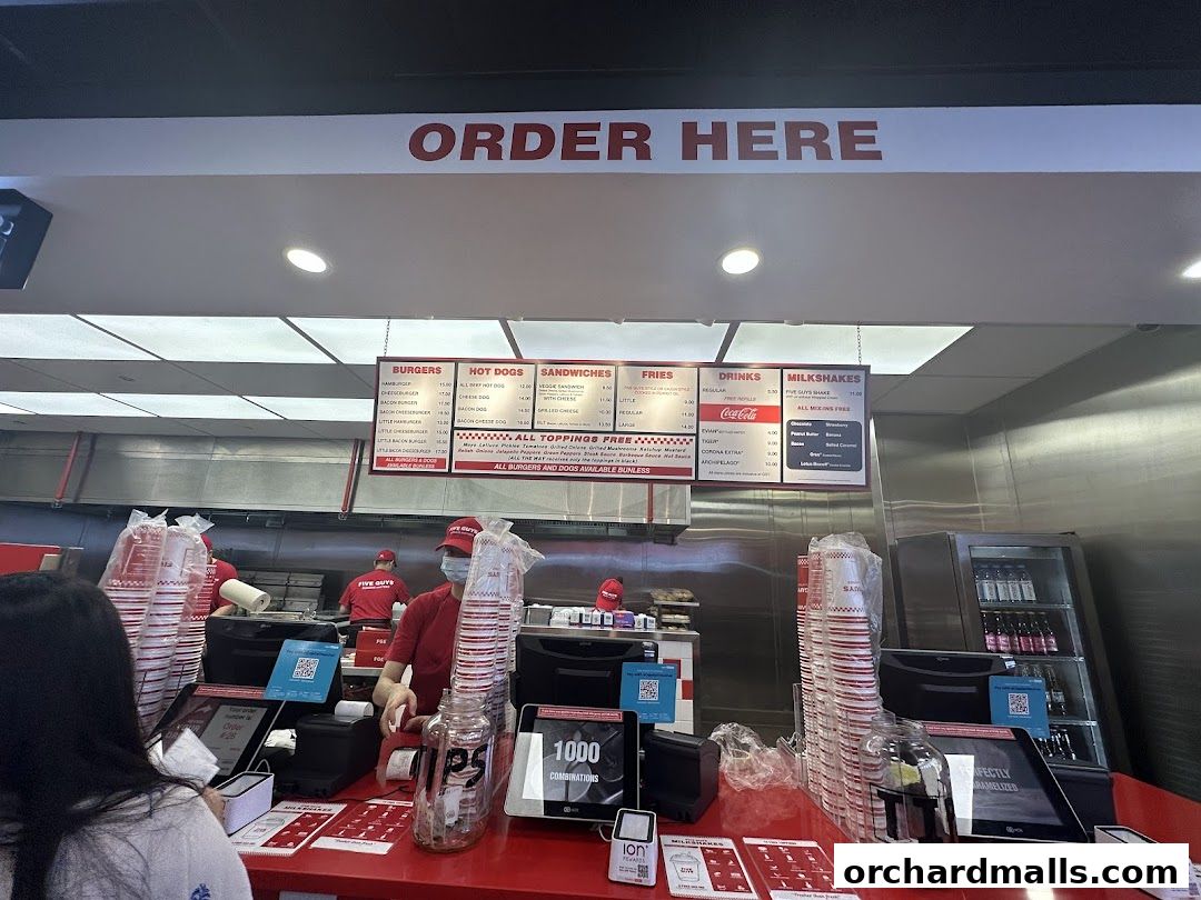 A Five Guys restaurant counter with a menu board displaying burgers, hot dogs, sandwiches, fries, drinks, and milkshakes.