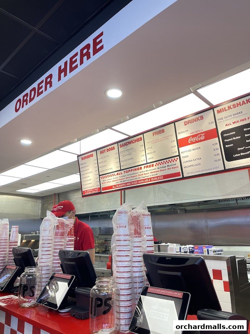 A Five Guys restaurant counter with a menu board displaying burgers, hot dogs, sandwiches, fries, drinks, and milkshakes.