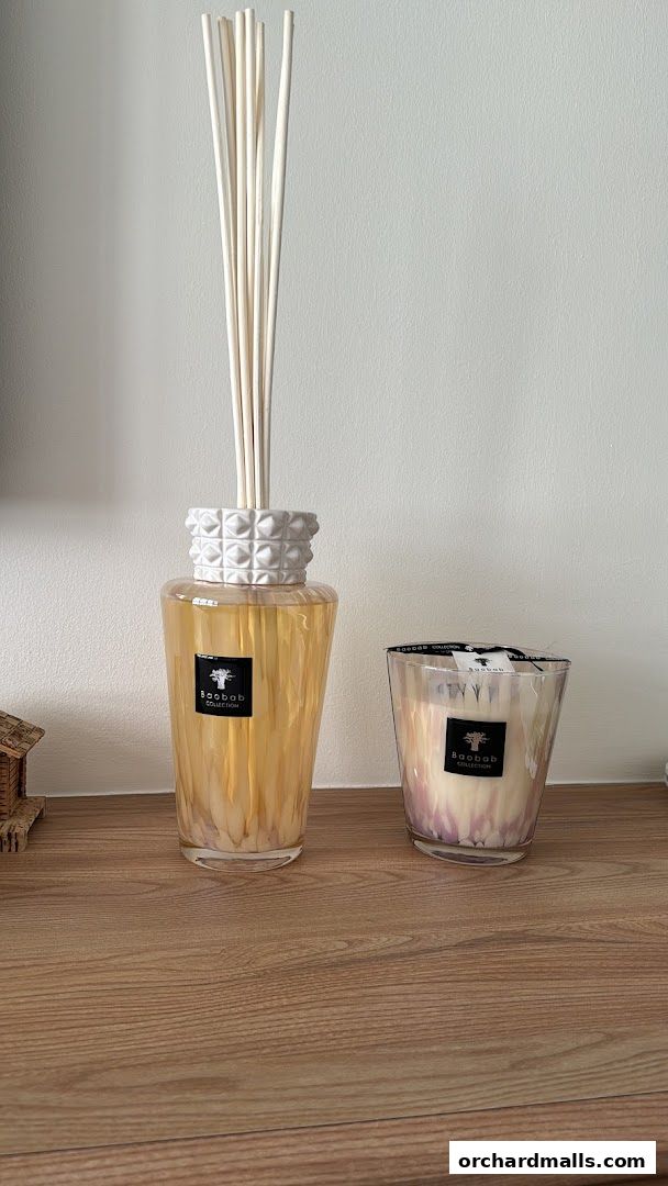 A diffuser and a candle from Baobab Collection on a wooden surface.