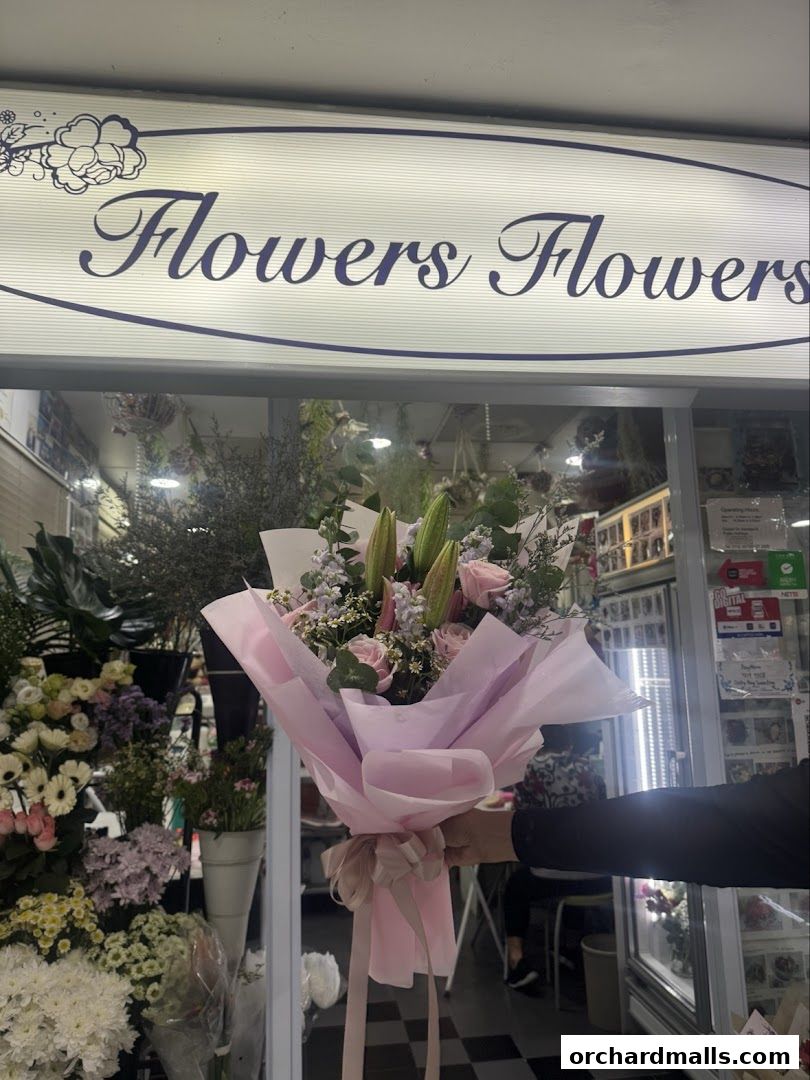 A person holds a bouquet in front of a flower shop with the name 'Flowers Flowers' above.